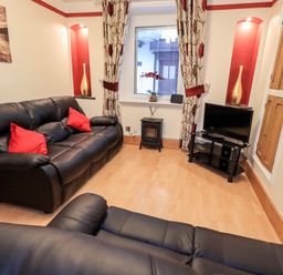 A living room with black leather sofas red pillows a television on a stand and curtains at Granary Nook in Windermere