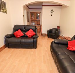 A living room with black leather sofas red cushions a wooden cabinet and a wall clock at Granary Nook Windermere