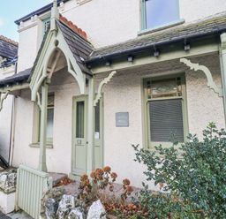Front entrance of a house with a wooden porch and green door and window frames at Greta Mill in Keswick