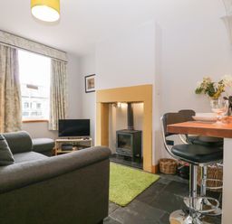A living area with a sofa television and wood stove next to a kitchen counter with bar stools at Banks Place in Keswick