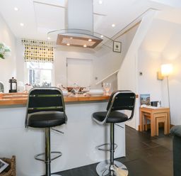 A kitchen area with two black bar stools at a wooden counter and a lamp next to nested wooden tables at Banks Place in Keswick