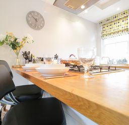 A kitchen with a wooden countertop stools bowls glasses a gas stove and a window with patterned blinds at Banks Place in Keswick