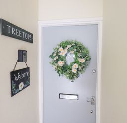 A gray door with a flower wreath hanging on it and two signs on the wall next to it at Tree Tops View in Bowness-On-Windermere