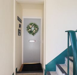 An indoor stairway with green railings near a grey door decorated with a floral wreath at Tree Tops View in Bowness-On-Windermere
