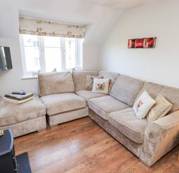 A living room with a beige sectional sofa and cushions next to a window and a wall-mounted TV at Tree Tops View in Bowness-On-Windermere