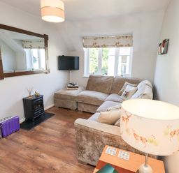 A living room with a corner sofa a wall-mounted TV a large mirror and a lamp on a side table at Tree Tops View in Bowness-On-Windermere