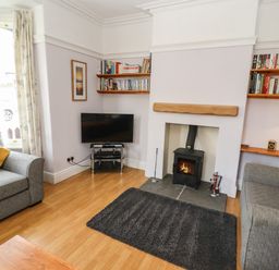 A living room with two grey sofas a wood burning stove television and bookshelves at Pelham House in Keswick