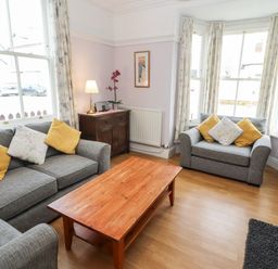 A sitting room with grey sofas yellow and floral cushions a wooden coffee table and a wooden sideboard with a lamp at Pelham House in Keswick