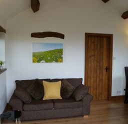 A living room with a brown sofa with cushions a wooden door a dining table with chairs and wall lights at Buttercup Cottage in Catterlen