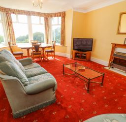A living room with a sofa a glass coffee table a dining table with chairs a television and a fireplace at Low Skelgill in Troutbeck
