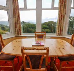A dining area with a wooden table and four chairs by large windows with curtains at Low Skelgill in Troutbeck