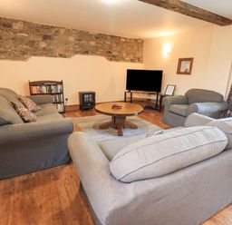 A living room with sofas a round wooden coffee table a television on a stand bookshelf and stone accent wall at Tithe Cottage in Cockermouth