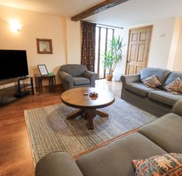 A living room with sofas a round coffee table a television and a plant at Tithe Cottage in Cockermouth