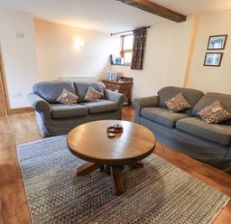 A living room with two grey sofas a wooden round coffee table and a rug at Tithe Cottage in Cockermouth