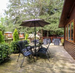 An outdoor wooden deck with a glass table and six chairs under an umbrella at Footprints Lodge in Windermere
