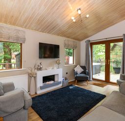 A living room with sofas a chair a black rug a wall-mounted television and glass doors at Footprints Lodge in Windermere