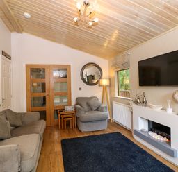 A living room with a sofa armchair wooden nested tables flat screen tv and modern fireplace at Footprints Lodge in Windermere