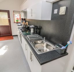 A kitchen with white cabinets black countertops a double sink and a wooden door at Long Crag Annexe in Ambleside