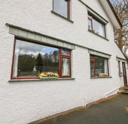 Exterior view of a white house with brown framed windows and flower boxes under two windows at Long Crag Annexe in Ambleside