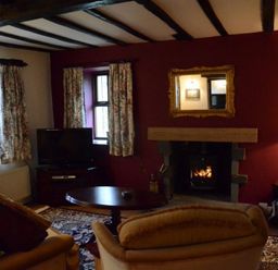 A living room with a fireplace a television floral curtains and wooden beams at Greety Gate House in Foxfield