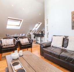A living space with black leather sofa and chairs near a wooden coffee table and kitchen area at Sky View in Keswick