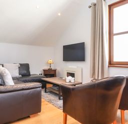 A living room with a black leather sofa black chairs wooden coffee table and wall mounted television at Sky View in Keswick