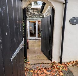 A black wooden gate entrance leading to a stone patio and glass doors with a white exterior wall showing a sign for Walkers Rest 21 at Walkers Rest in Windermere