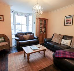 A living room with two leather sofas a wicker chair a wooden coffee table a wooden cabinet and a chandelier at Walkers Rest in Windermere