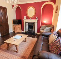 A living room with a fireplace a wooden coffee table a television a brown leather sofa and a wicker chair at Walkers Rest in Windermere