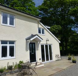 An exterior view of a cream colored house with black door and white windows patio furniture and plants on a stone patio at Eribel Cottage in Threlkeld