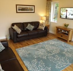 A living room with leather sofas a blue floral rug and a wall mounted television at Eribel Cottage in Threlkeld