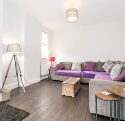 A living room with a grey sectional sofa with purple cushions a wooden coffee table and two side tables at Latrigg House in Keswick
