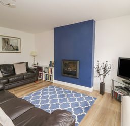A living room with leather sofas a blue patterned rug a wall-mounted fireplace and a television at Derwentwater Apartment Keswick