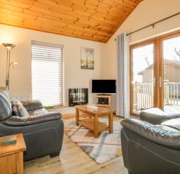 A living room with black leather sofas wooden coffee table TV and glass door at Holmedell in Greystoke