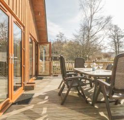 An outdoor wooden deck with a dining table and chairs outside a wooden building at Holmedell in Greystoke