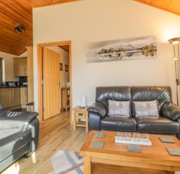 A living room with leather sofas a wooden coffee table floor lamp and a kitchen area at Holmedell in Greystoke