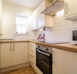 A kitchen with white cabinets a wooden countertop an oven a stove a microwave and a window at Siskin Keswick