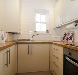 A small kitchen with white cabinets wooden countertops a toaster kettle oven and a window at Siskin in Keswick