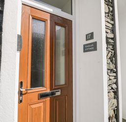 A wooden front door with glass panels and a letterbox at 17 Raglan Cottage in Bowness-on-Windermere