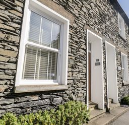 Stone exterior of a house with windows doors and small plants along the wall at Raglan Cottage in Bowness-on-Windermere