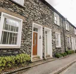 A stone exterior terrace with multiple doors and windows along a narrow street at Raglan Cottage in Bowness-on-Windermere