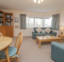 A living room with blue sofas a wooden coffee table and dining table with chairs at Treetops in Windermere