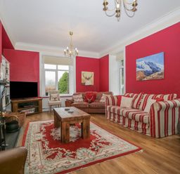 A living room with red walls striped and leather sofas wooden coffee table rug and fireplace at The Old Vicarage in Keswick