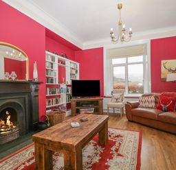 A living room with a wooden coffee table a fireplace bookshelf and a brown leather sofa at The Old Vicarage in Keswick