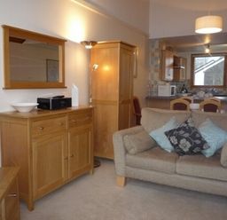 A living area with a beige sofa and cushions wooden cabinets and a kitchen in the background at 5 Keswick Bridge in Keswick