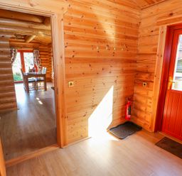 An interior view of a wooden cabin with a door leading to a dining area and a red door opening to a garden at Ash Lodge in Greetham Rutland
