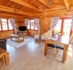 A living room and dining area with floral curtains wooden furniture and a television at Ash Lodge in Greetham Rutland