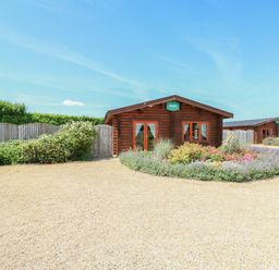 A gravel driveway with a flower bed in front of wooden lodges at Ash Lodge in Greetham Rutland