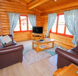 A living room with brown leather sofas a wooden coffee table a TV on a wooden stand and windows with blue curtains at Yew Lodge in Greetham Rutland