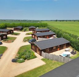 An aerial view of multiple wooden lodges with patios and parked cars surrounded by green fields at Yew Lodge in Greetham Rutland